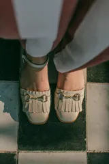Sandalias de cuero color celeste, con punta cerrada, flecos frontales y detalle de estribo metálico dorado. Tienen tira ajustable al tobillo y suela plana con pequeño taco.