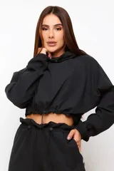 Conjunto deportivo de dos piezas compuesto por un buzo cropped de cuello alto con cordón ajustable y un pantalón estilo clochard de corte holgado con cintura elástica regulable y bolsillos laterales. Ambas prendas están confeccionadas en tejido técnico ligero con acabado suave al tacto.