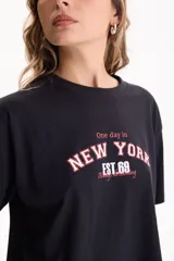 Remera cropped de algodón color negro con diseño gráfico estampado en el frente con las inscripciones 'One day in', 'NEW YORK' y 'EST. 69'. Presenta mangas cortas y calce cómodo.
