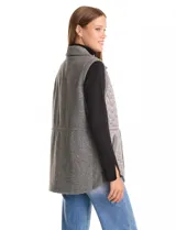 Chaleco gris de diseño híbrido, con frente capitoneado de patrón ondulado y espalda de tejido de punto. Presenta cuello con solapa, cierre frontal con botones a presión metálicos, cordón de ajuste en la cintura y bajo curvo.