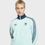 Campera deportiva Adidas Originals de la selección de Alemania, color verde agua con detalles en azul marino. Presenta cuello alto, cierre frontal completo, bolsillos laterales y las icónicas tres tiras de la marca en las mangas. Incluye el logo del trébol y el escudo de la federación alemana en el pecho.