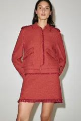 Chaqueta corta de tweed en color rojo, con cuello solapa, manga larga y bolsillos frontales con solapa. Presenta detalles deshilachados en los bordes y cierre frontal con cremallera oculta.