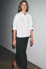Camisa blanca de algodón con cuello solapa, detalle de pliegues en el delantero y mangas tres cuartos abullonadas terminadas en puño. Cierre frontal con botones ocultos.