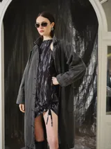 Trench largo de denim gris lavado, de silueta recta y amplia, con solapas amplias, mangas largas y botonadura frontal.