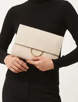 Cartera tipo clutch de cuero vegano color beige, con solapa frontal, herraje metálico circular dorado y correa de cadena desmontable.