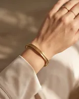 Pulsera tipo esclava rígida de acero con baño de oro, con diseño de banda central texturizada y bordes lisos.