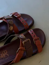 Sandalias de cuero marrón, con diseño de triple tira con hebillas, detalles de tachas y apliques de pelo con estampado animal print.