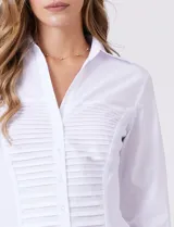 Camisa blanca entallada de algodón con escote en V y cuello con solapa. Presenta un diseño frontal con alforzas horizontales en la pechera y mangas tres cuartos con puños anchos rebatibles.