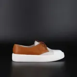 Zapatillas acordonadas tipo championes, confeccionadas en cuero color suela y blanco, con base de goma blanca.