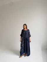 Vestido largo azul oscuro con diseño asimétrico que combina un lado liso con un lado estampado de hojas, manga corta y bolsillo frontal aplicado.