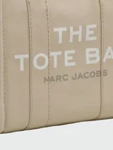 Bolso tipo tote de Marc Jacobs, confeccionado en lona resistente color beige. Presenta el logo estampado en contraste en el frente, doble asa superior y cierre superior con cremallera.