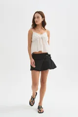 Minifalda de jean negra con diseño cruzado, cierre de hebilla metálica y detalle de tablones plisados en el lateral.