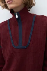 Sweater de punto color crudo con cuello alto y cierre frontal parcial. Presenta detalles de vivos en color marrón en el cuello, hombros y ruedo, con diseño de manga larga.