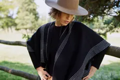 Ruana de tejido de punto en color negro con diseño de rayas verticales blancas y terminaciones con flecos en los bordes.