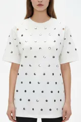 Remera holgada de manga corta y cuello redondo, color blanco, decorada con tachas plateadas distribuidas por toda la prenda.