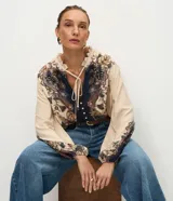 Blusa tipo bata de viscosa con estampa floral estilo paisley. Presenta cuello alto con detalle de volados, cierre frontal con botones y lazo ajustable en el escote. Posee mangas largas abullonadas con puños elásticos.