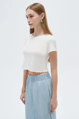 Remera crop de manga corta en tejido de poliamida al cuerpo, de color blanco, con cuello redondo y terminaciones con volados sutiles en mangas y ruedo.