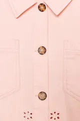 Cazadora color rosa pálido, de cuello solapa y manga larga. Tiene bordados perforados a tono en el ruedo y cierre frontal con botones color madera.