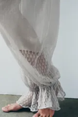 Pantalón abombacho semitransparente de tejido de encaje suave color gris, con tiro medio, cintura elástica y diseño con calados y volantes en los tobillos.