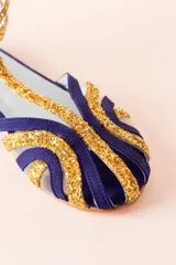 Sandalias tipo cangrejeras con rejilla en la punta y laterales combinados en ante morado y glitter dorado. Ajuste con hebilla en el tobillo. Fabricadas en España con interior de piel y suela de cuero. Cuentan con una cuña interna de 1,5 cm.