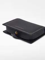 Monedero negro de piel de cordero con estructura rígida, cierre de broche, tarjetero interior, pespunte decorativo a contraste y logo grabado.