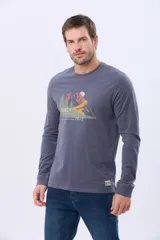 Remera de manga larga color gris oscuro, con cuello redondo y estampado frontal de un paisaje montañoso con árboles y un sol. Incluye el texto "LEGACY UNIVERSAL ADVENTURE" y "TRUE QUALITY SINCE 1972".