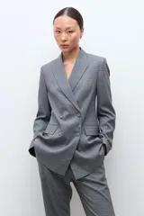 Blazer de corte sastre con doble botonadura frontal, solapas clásicas y bolsillos laterales con solapa. Presenta un diseño estructurado con estampado de microcuadros.