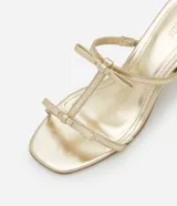 Sandalia mule dorada con punta cuadrada, tiras finas con detalle de lazos y tacón cuadrado mediano.