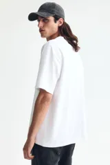 Remera blanca de manga corta, cuello redondo ribeteado y corte relajado con hombros caídos. Fabricada en punto liviano con fibra COOLMAX.