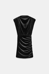 Vestido corto de cuello barco y mangas cortas con hombreras, confeccionado en tejido satinado negro. Presenta un diseño con frunces laterales y en la parte superior, aportando un efecto drapeado.