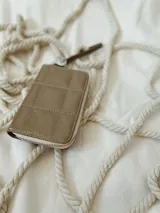 Billetera de cuero color visón, de tamaño intermedio, forrada, con reparticiones internas y cierre metálico.