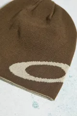Gorro beanie de punto fino, color marrón con diseño jacquard del logotipo Ellipse en tono crema. Modelo reversible de silueta sencilla.