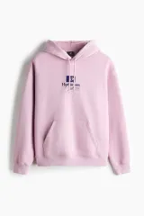 Canguro de algodón con capucha y cordones ajustables, diseño de hombros caídos y bolsillo frontal tipo canguro. Presenta un estampado gráfico en el pecho y puños acanalados.