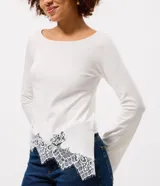 Blusa de algodón con cuello bote y mangas largas. Presenta un diseño asimétrico en el bajo decorado con un delicado detalle de encaje.