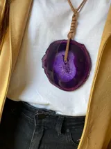 Collar con dije de piedra ágata blanca y marrón, con forma circular irregular y agujero en el centro. El dije está sujeto con un cordón fino de cuero marrón.