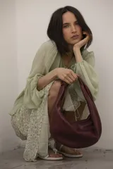 Cartera tipo hobo de cuero color borgoña, con cierre superior y asa anudada.