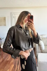 Camisa cropped de cuero ovino color marrón oscuro/chocolate con efecto desgastado. Presenta cuello camisero, cierre frontal con cordones y cut-outs laterales en las mangas con cordones a juego.