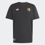 Remera negra de algodón con cuello redondo y mangas cortas. Presenta el logo del Trifolio de Adidas en blanco en el pecho derecho y un parche circular con manos entrelazadas en colores rasta en el pecho izquierdo. Incluye un pequeño parche rectangular en la parte inferior derecha.