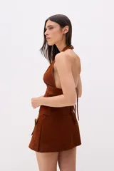 Top largo negro de cuero, estilo chaleco, con escote halter profundo y abertura frontal sujeta por dos tiras horizontales a la altura de la cintura.