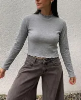 Remera de morley de algodón color gris, de manga larga, con cuello alto y terminaciones con borde fruncido en cuello, mangas y ruedo.
