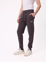 Pantalón tipo jogger de color gris oscuro, con cintura elástica ajustable mediante cordón, puños elásticos en los tobillos y logo de la marca estampado en la pierna izquierda.
