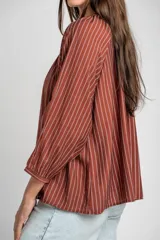 Blusa de manga larga con diseño a rayas verticales, cuello redondo con pequeña abertura frontal abotonada y mangas con puños elásticos.