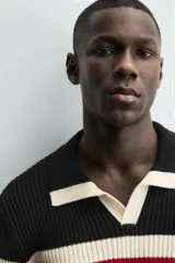 Polo de punto tejido con cuello solapa y abertura frontal, manga larga y calce relajado. Presenta un diseño a rayas horizontales anchas en negro y beige, con una fina línea roja separando las franjas.