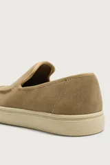 Mocasín casual de hombre confeccionado en piel con acabado de gamuza. Presenta un diseño de horma redonda con detalle de costura en el empeine y suela de goma a contraste con textura.