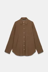 Camisa oversize de algodón con cuello solapa, manga larga y cierre frontal con botones. Presenta un bolsillo de plastrón en el frente y un diseño de corte amplio con ruedo redondeado.