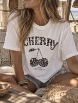 Remera blanca de manga corta y corte holgado con estampado frontal de cerezas y la palabra "CHERRY" en animal print, acompañada del texto "HAPPY HAVE A NICE DAY".