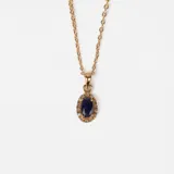 Collar de oro 18k con cadena fina de eslabones y dije ovalado central que presenta un zafiro azul rodeado por pequeños brillantes.