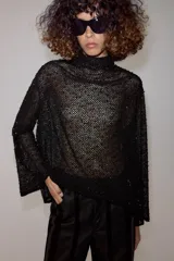 Camisa de hilatura con viscosa color negro, con cuello subido y manga larga ancha. Presenta aplicaciones de abalorios combinados a tono en toda la prenda y bajo recto.