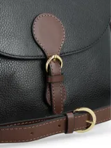 Cartera tipo bandolera de cuero negro con detalles en color marrón. Presenta una solapa frontal con cierre de hebilla decorativa y broche a presión, correa ajustable y bordes contrastantes.
