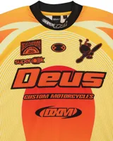 Remera de motocross manga larga marca Deus Ex Machina, en tonos azules con gráficos estampados en color rosa y negro. Presenta cuello redondo, puños elásticos y diseño deportivo con logotipos de la marca.